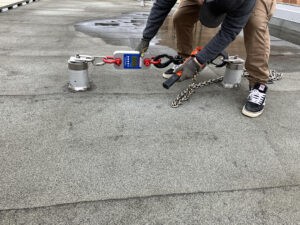 a person holding a chain with a roof anchor pull tester attached to it